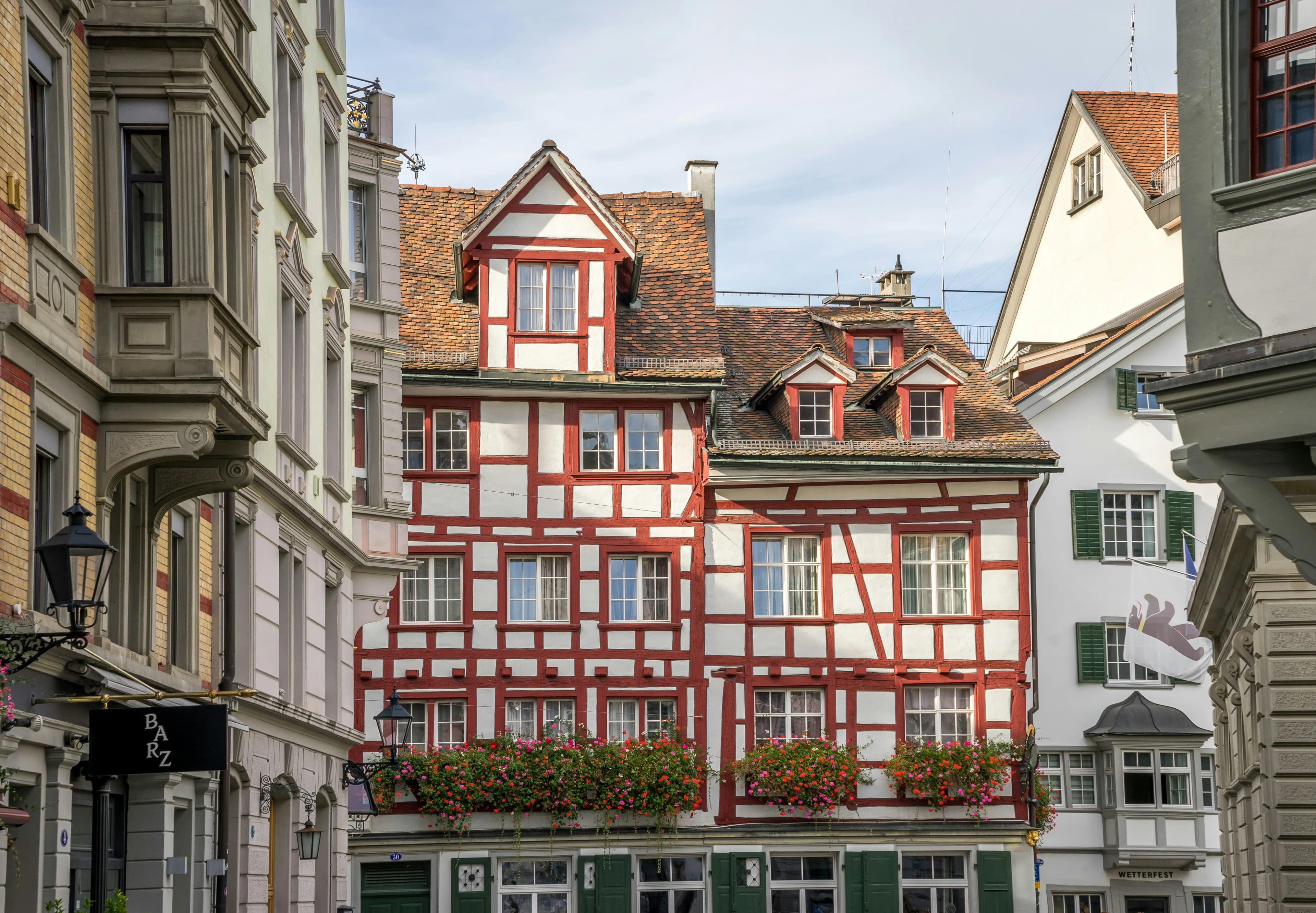 A historic half-timbered house with a red and white facade and decorated with flower boxes is a beautiful sight in a city street.