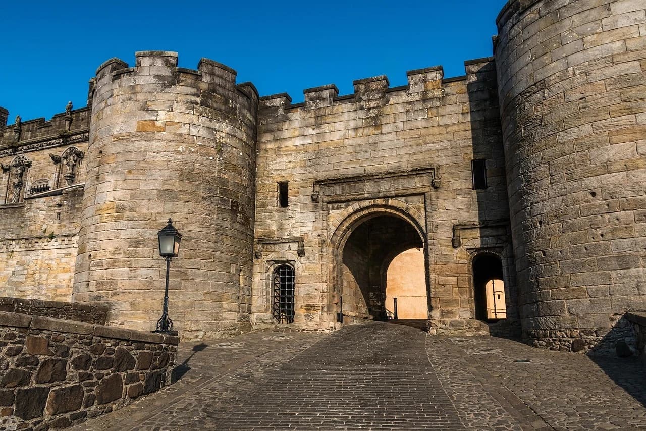 The historic stone gateway of Stirling Castle, with its fortified walls and a cobblestone street, is a grand entrance to the fortress.
