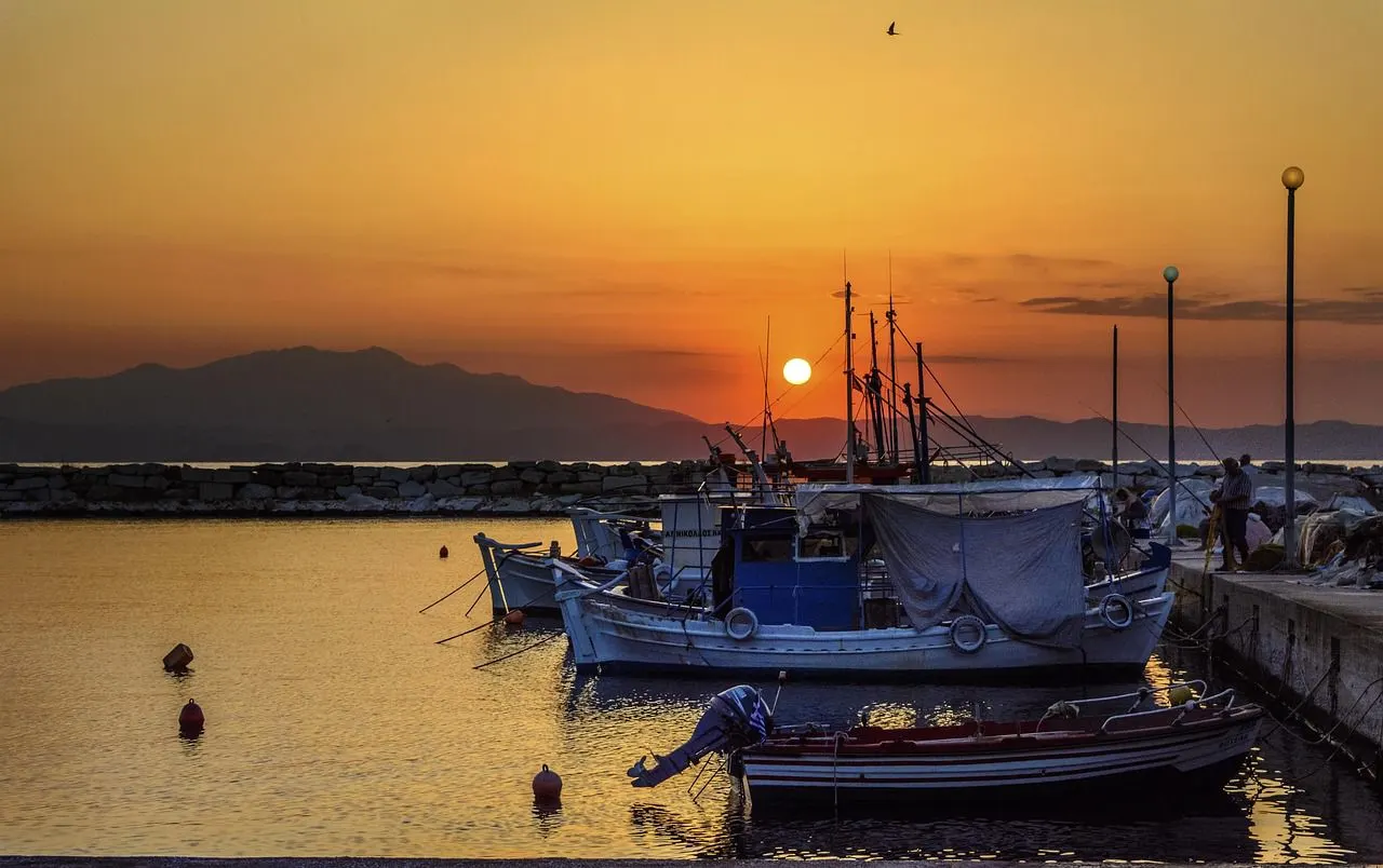A small, picturesque bay with a fishing boat moored in the shallow water is bordered by a sandy beach and a rocky coastline.