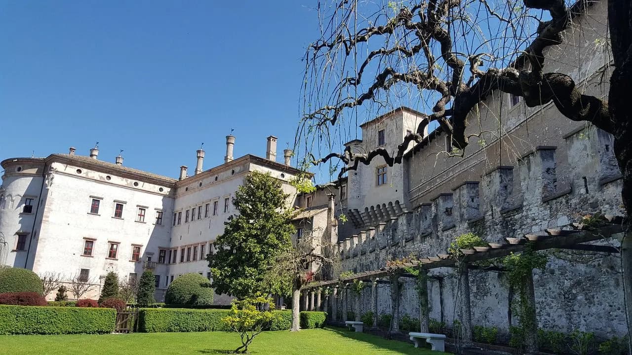 The historic city of Trento is beautifully illuminated at dusk, with the lights of the buildings glowing and the Adige River flowing through.