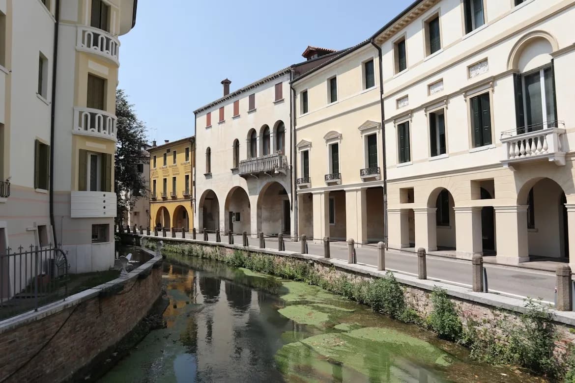 A historic stone bridge with a few small arches spans a tranquil canal in Treviso.