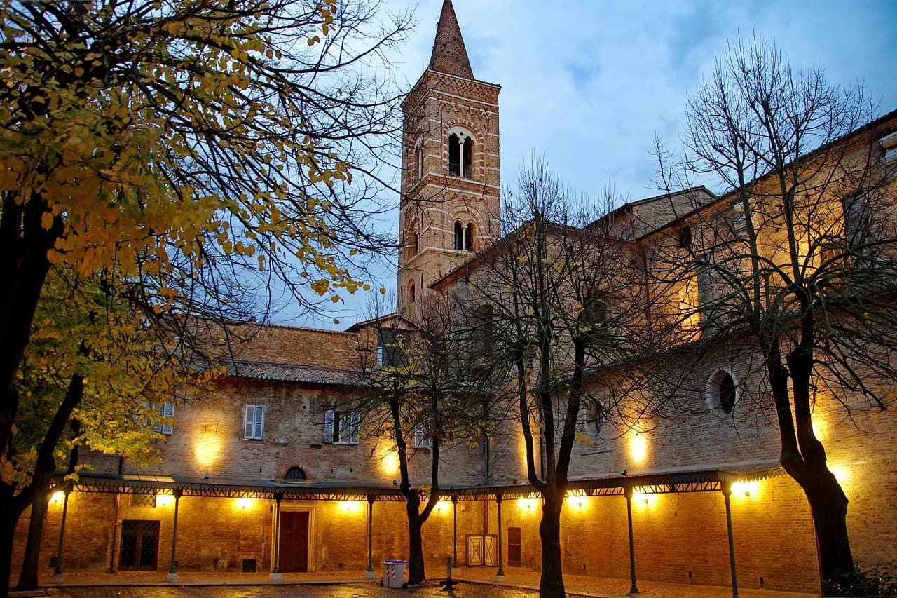 A panoramic view of the historic city of Urbino shows a mix of traditional red-tiled roofs and the elegant buildings of the Palazzo Ducale.