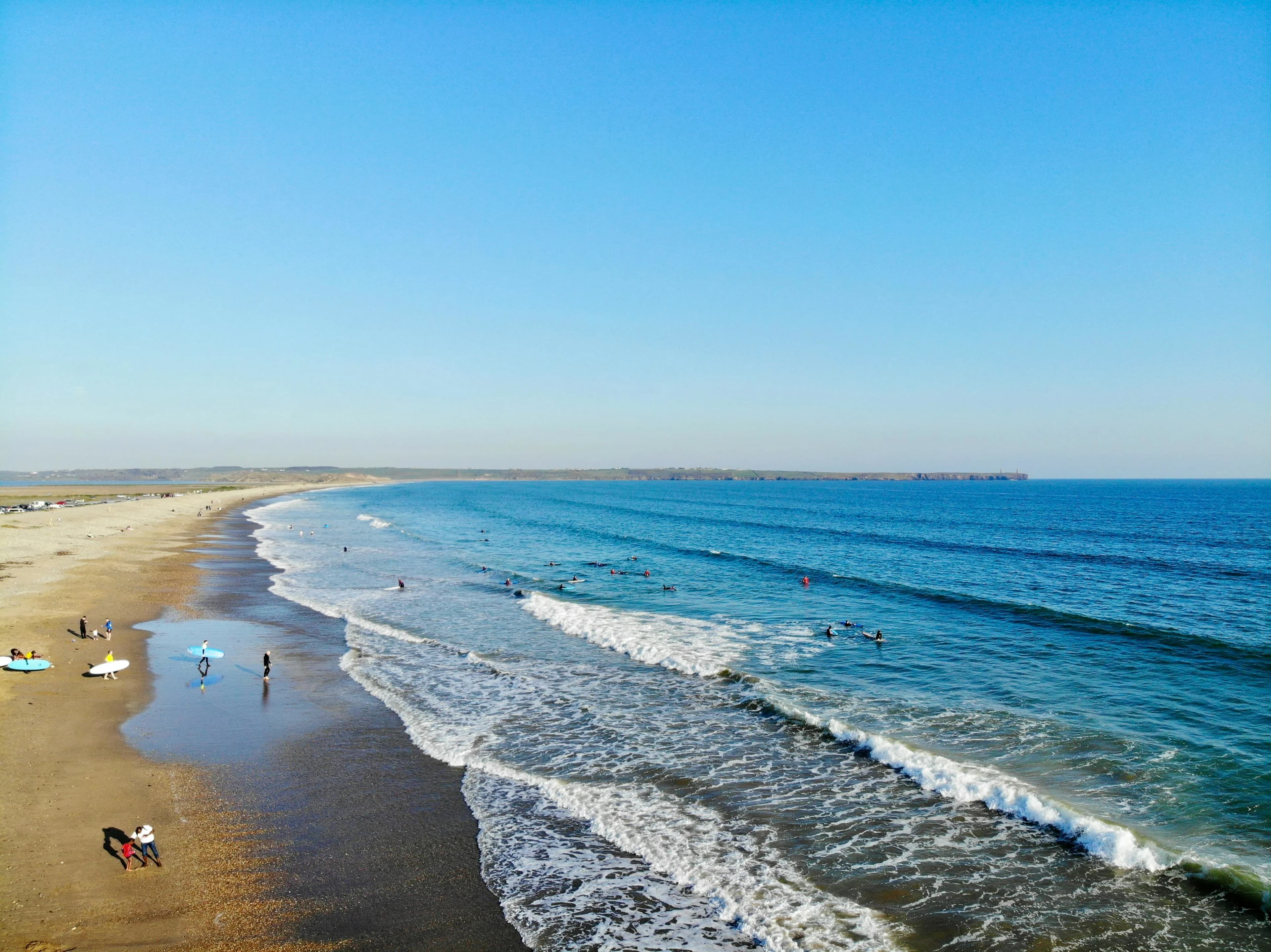 An expansive view of a sandy beach with people surfing and swimming in the waves.