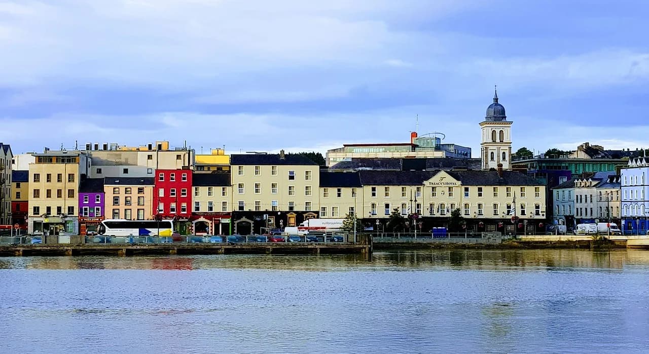 A panoramic view of the city of Waterford from across the river, showing colorful buildings lining the waterfront.
