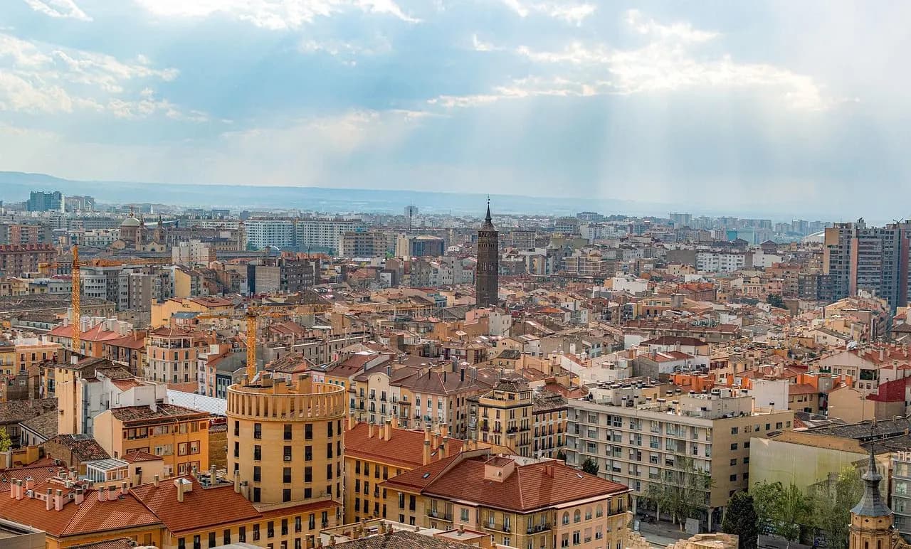 A panoramic view reveals the urban landscape of Zaragoza, characterized by a mix of historic and modern buildings under a beautiful sky.