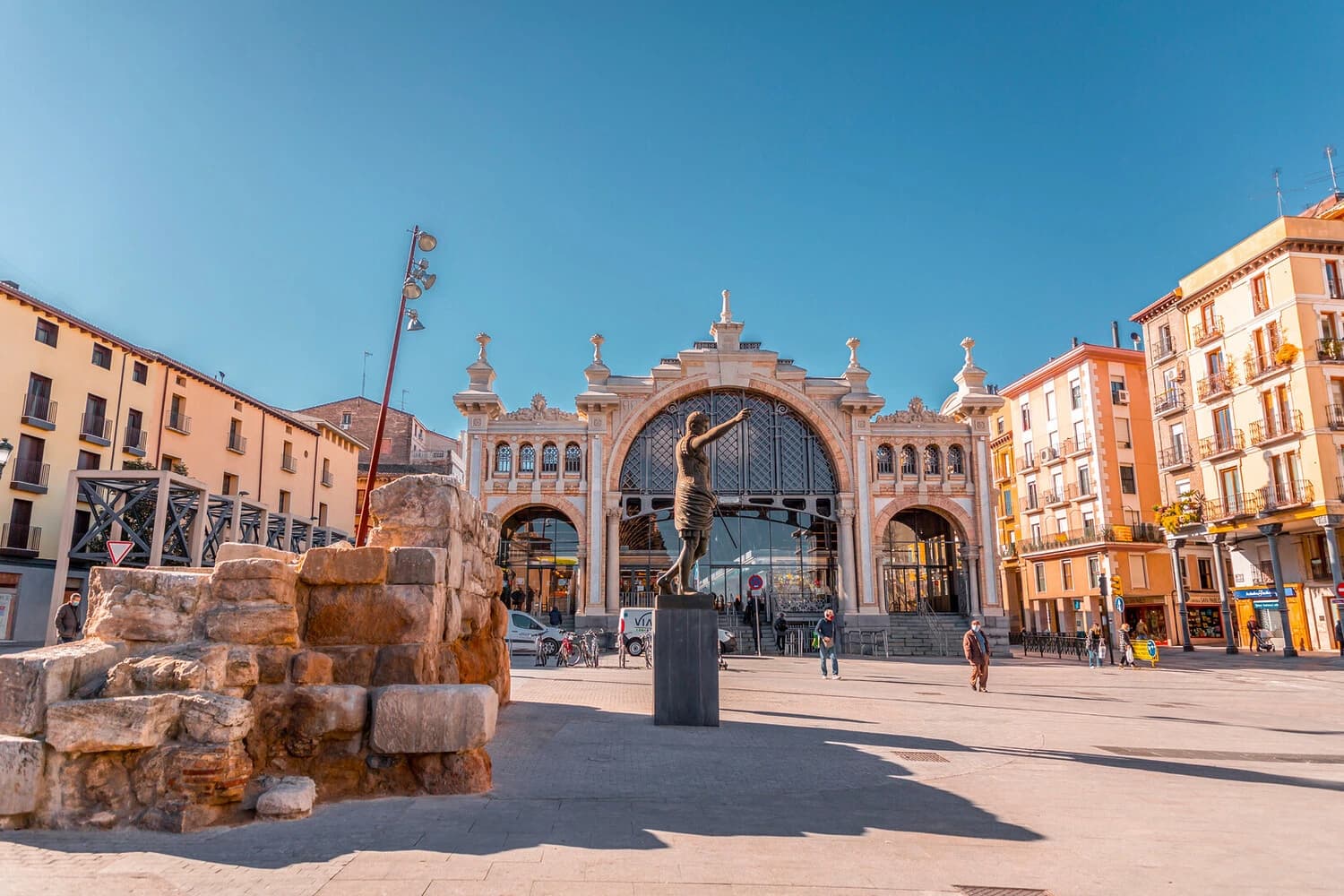 A statue of Caesar Augustus stands in front of the Mercado Central, Zaragoza's central market, on a sunny day.